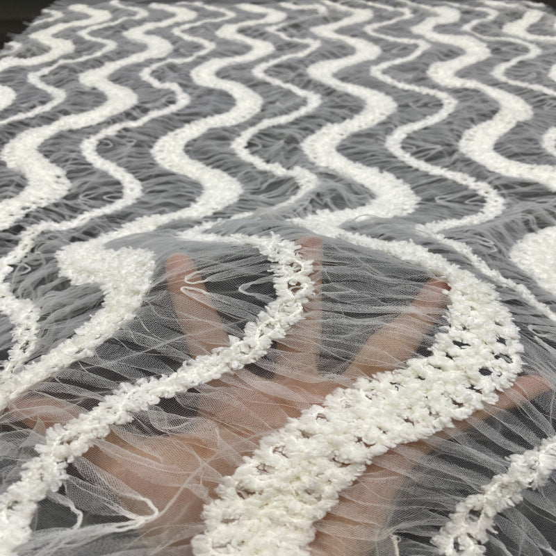 Sheer white sequined lace held up to show translucent ground and embroidered wavy lines
