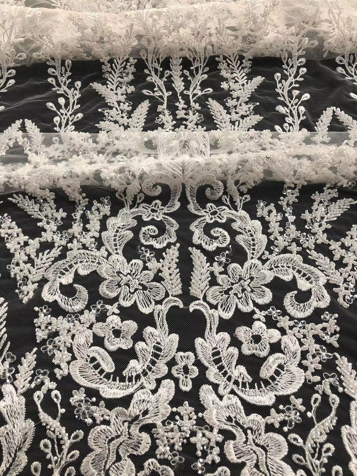 Rolled black mesh fabric showing dense white beaded and sequined floral decoration