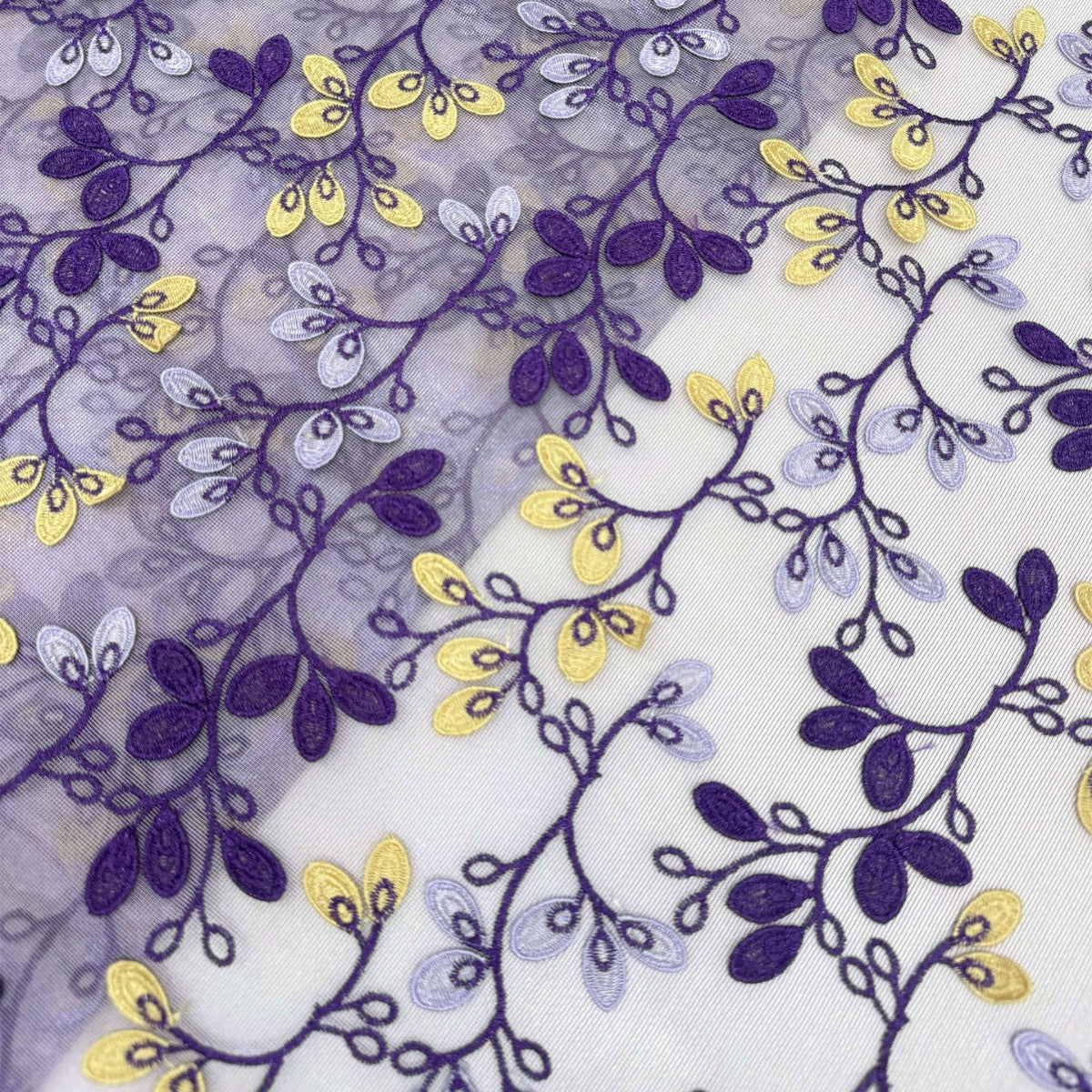 Close-up of purple and yellow embroidered vines and leaves across transparent chiffon