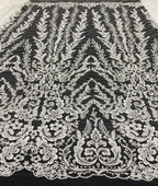 Close-up of ivory-white embroidered scrolling floral motifs on black mesh