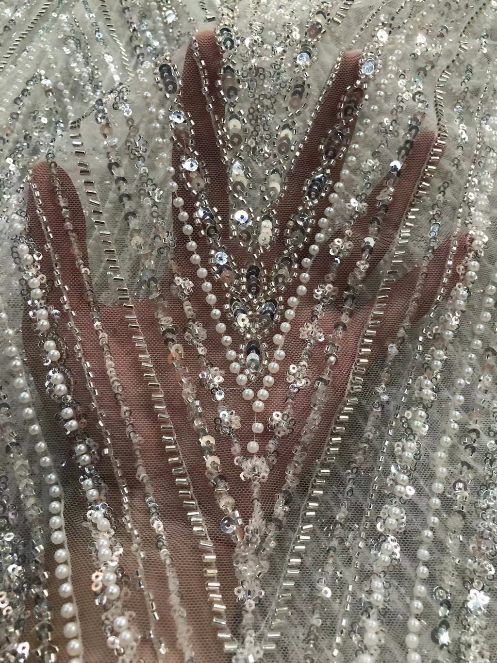 Close-up of silver beads and sequins forming radiating lines over a hand