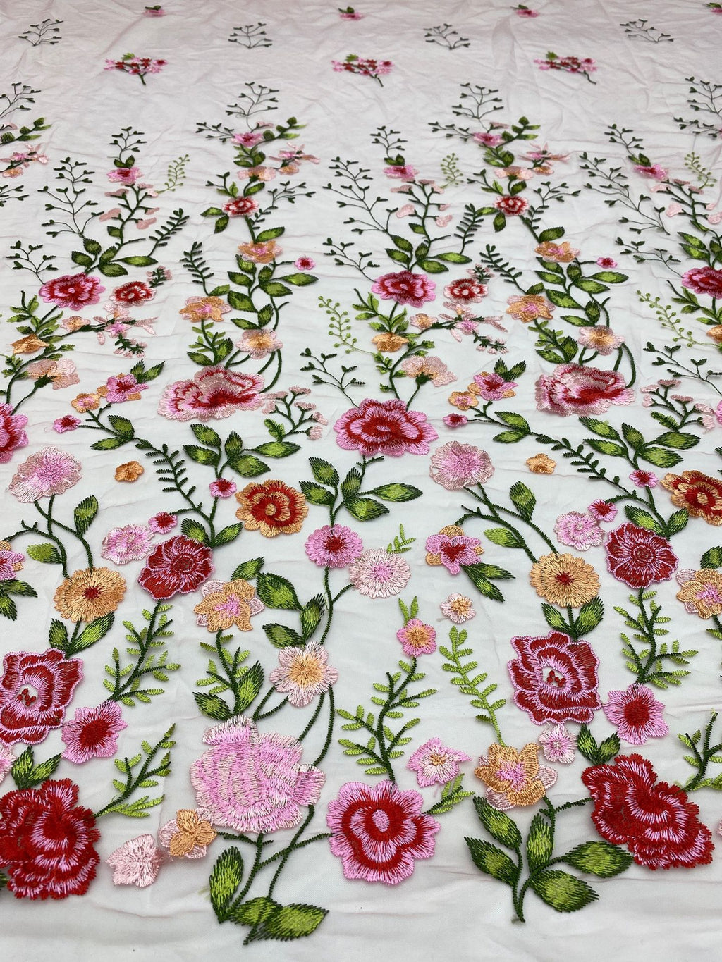 Close-up of multicolored rose and leaf thread embroidery on light sheer fabric