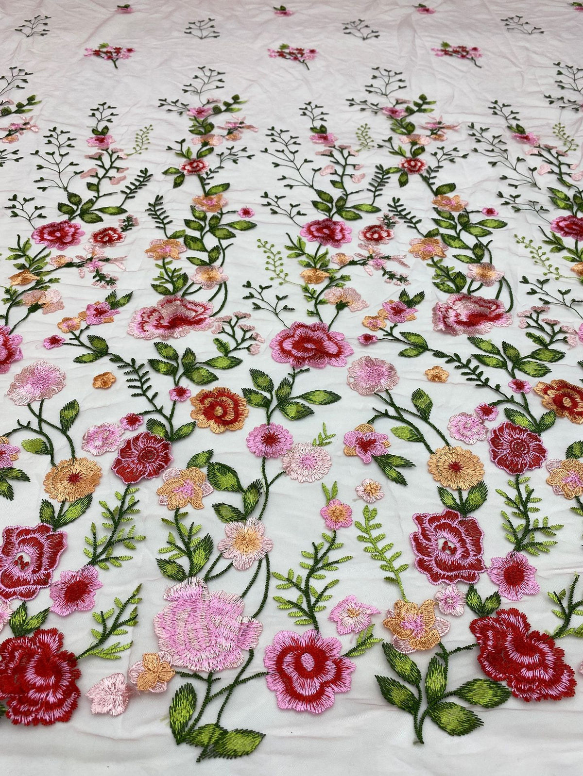 Close-up of multicolored rose and leaf thread embroidery on light sheer fabric