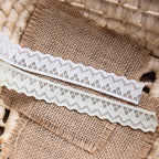 White geometric zigzag lace trim displayed against burlap with cut edges and narrow width