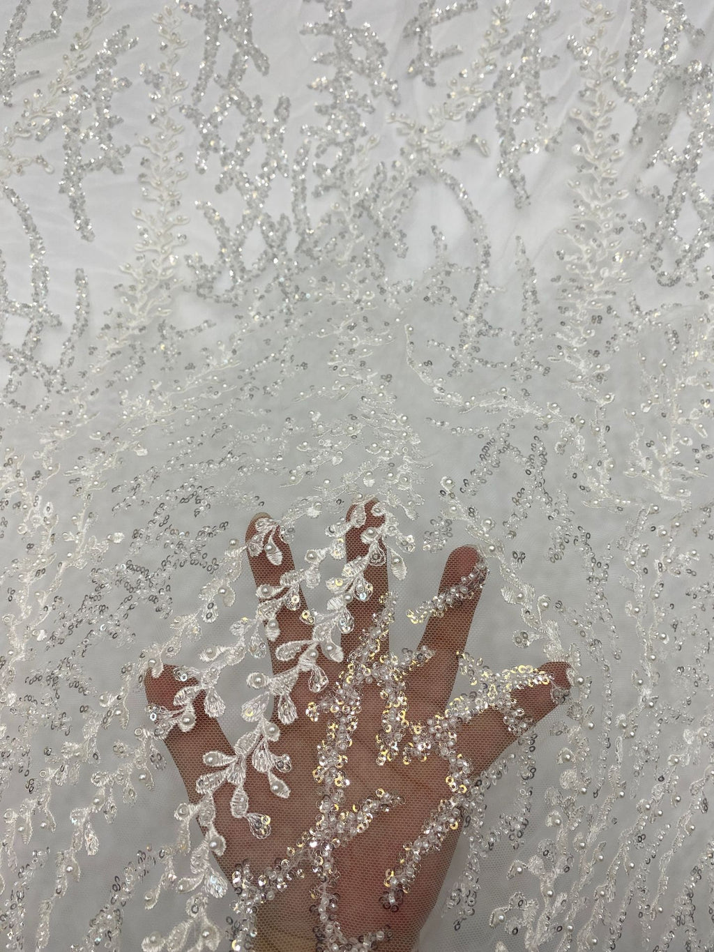 Hand holding pale sheer bridal fabric to show silver embroidered beaded motif scale