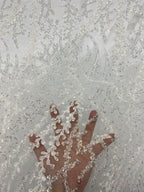 Hand holding pale sheer bridal fabric to show silver embroidered beaded motif scale