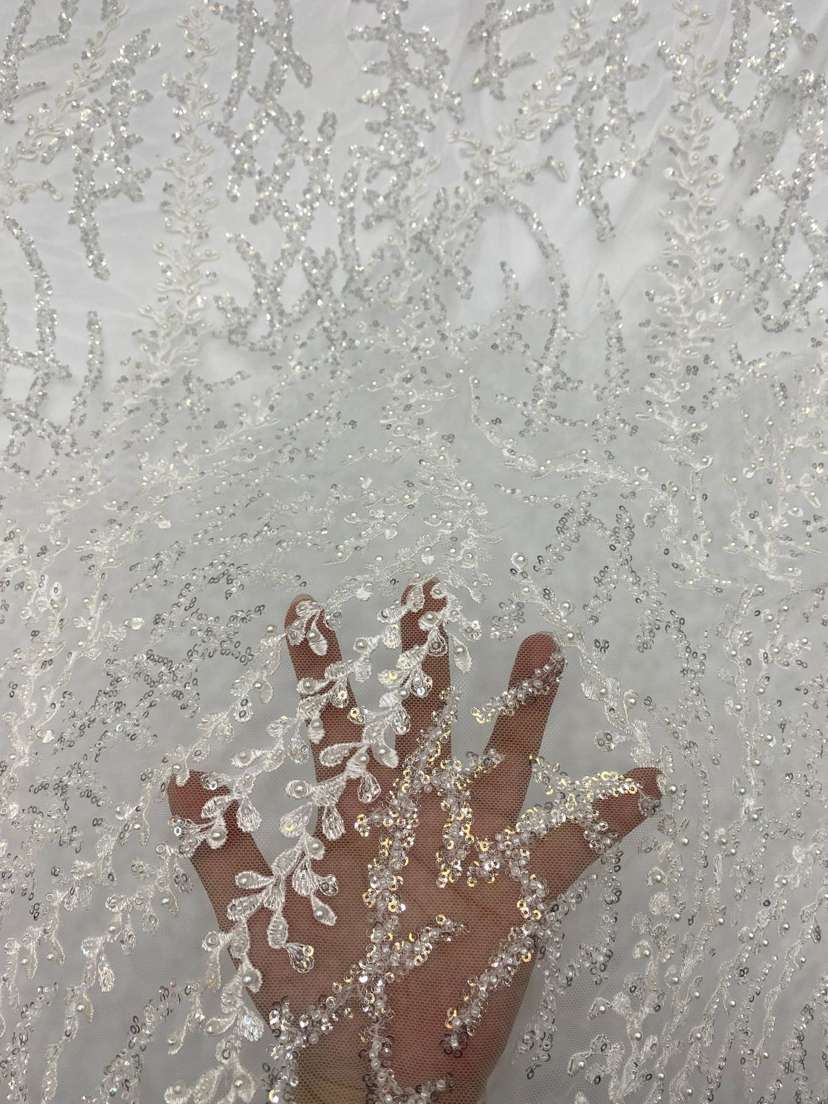 Hand holding pale sheer bridal fabric to show silver embroidered beaded motif scale
