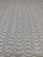 Close-up of repeated silver wave-shaped bead and sequin embroidery on pale sheer mesh