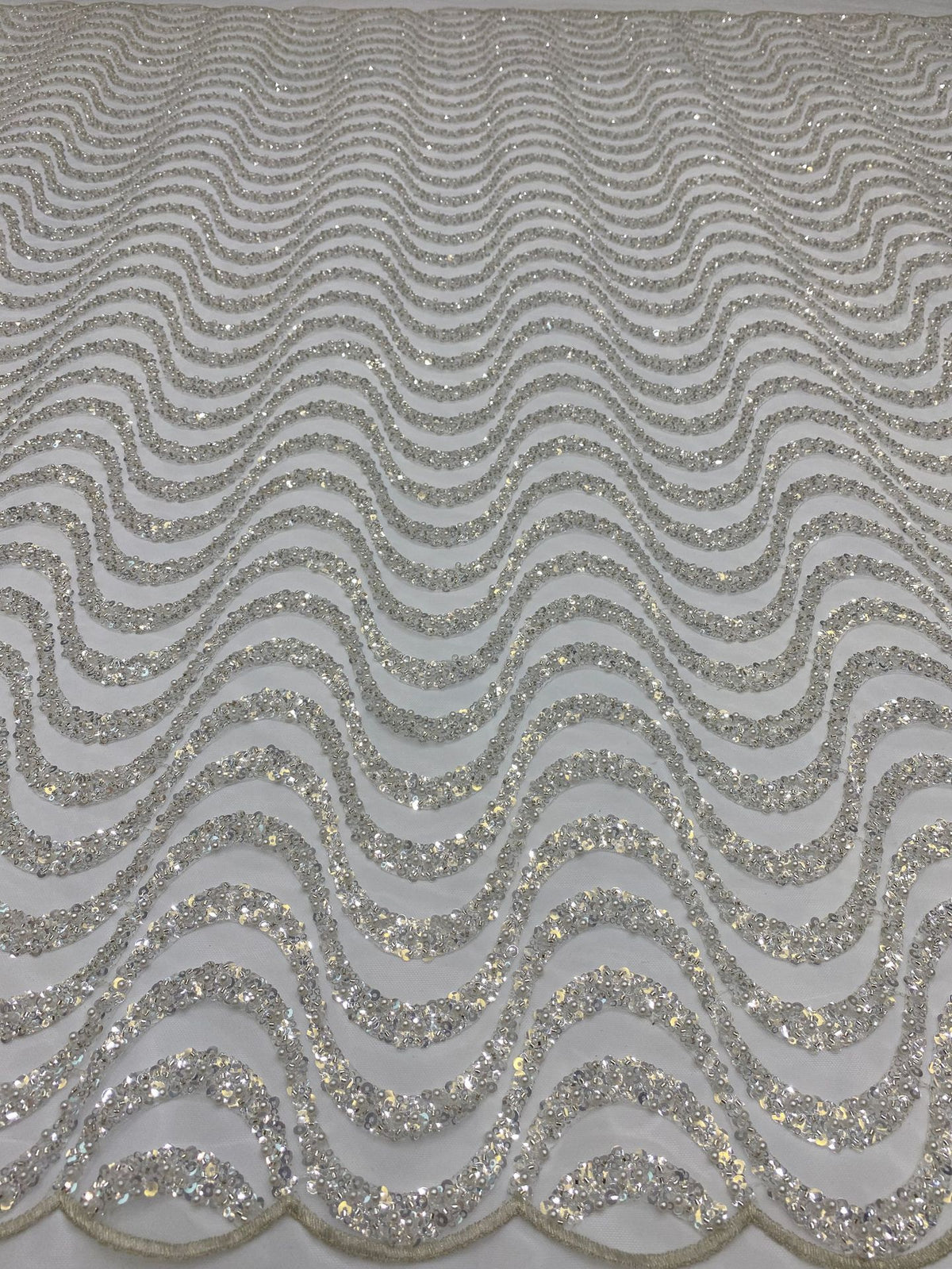 Close-up of repeated silver wave-shaped bead and sequin embroidery on pale sheer mesh