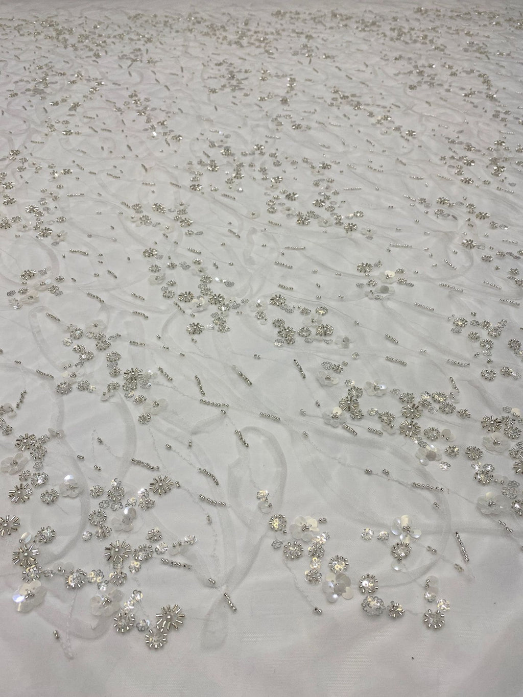 Close-up of ivory mesh with silver bead and sequin curving floral pattern