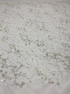 Close-up of ivory mesh with silver bead and sequin curving floral pattern