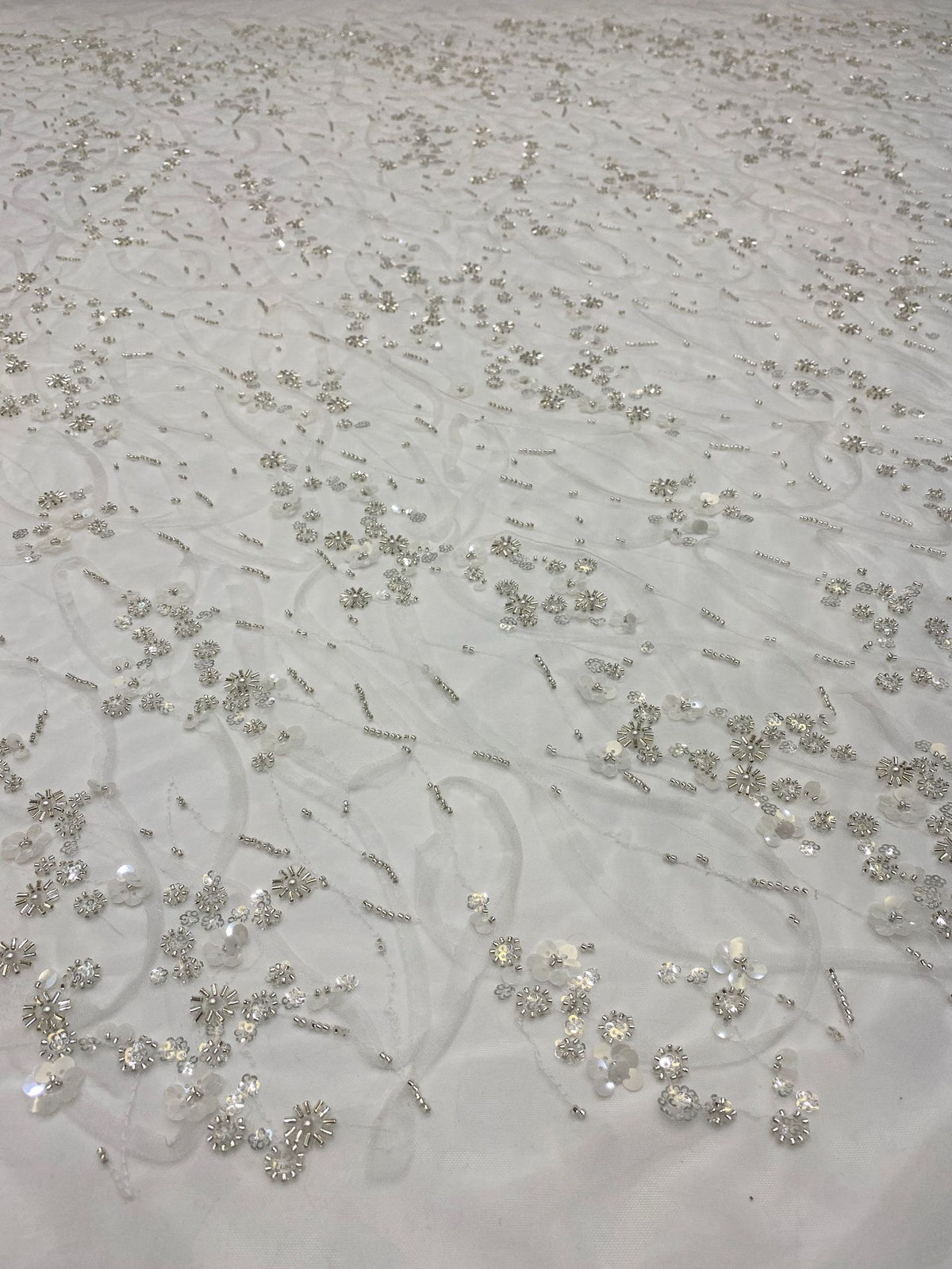 Close-up of ivory mesh with silver bead and sequin curving floral pattern