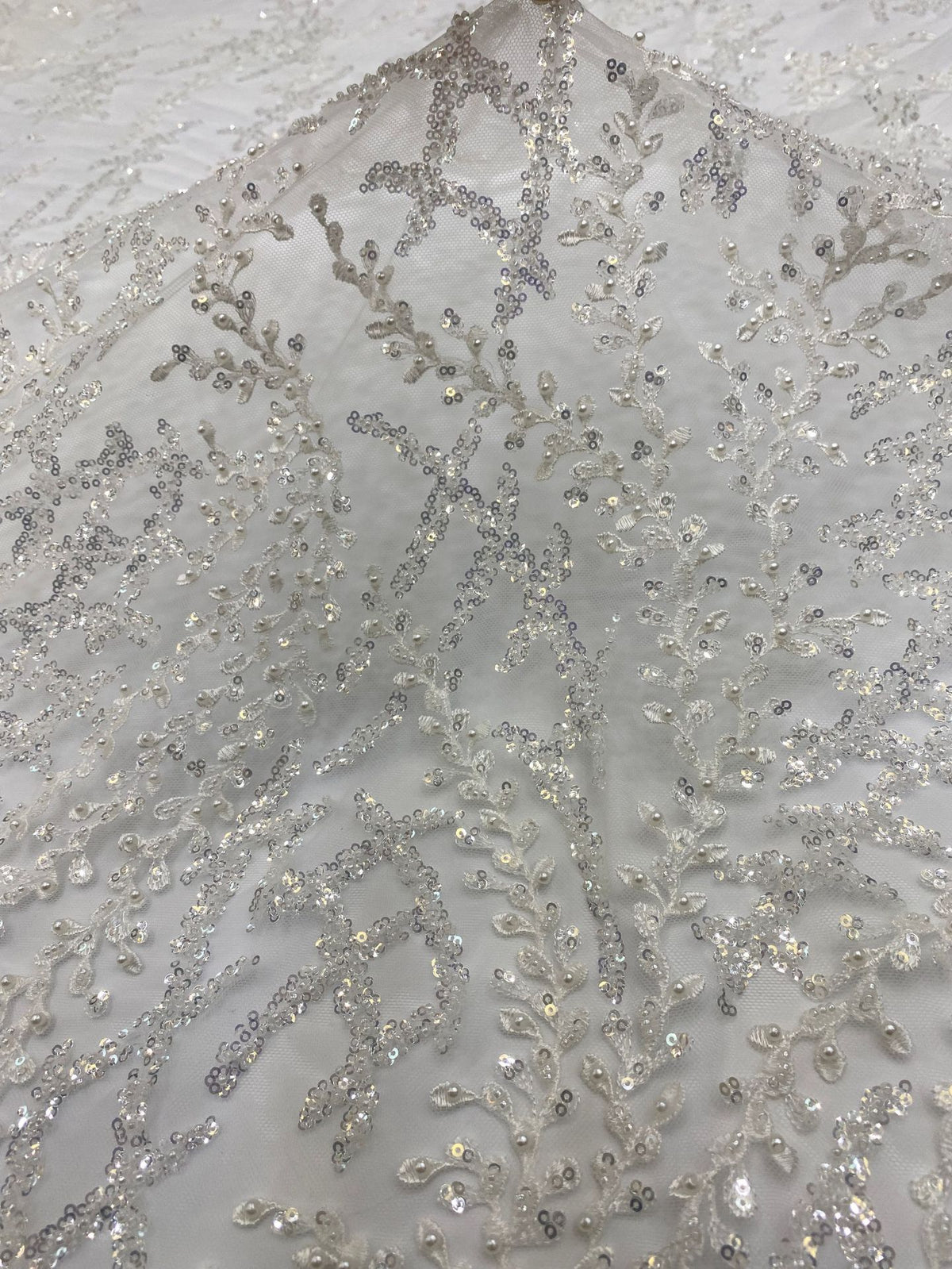 Close-up of silver bead and sequin embroidered swirls on ivory sheer fabric