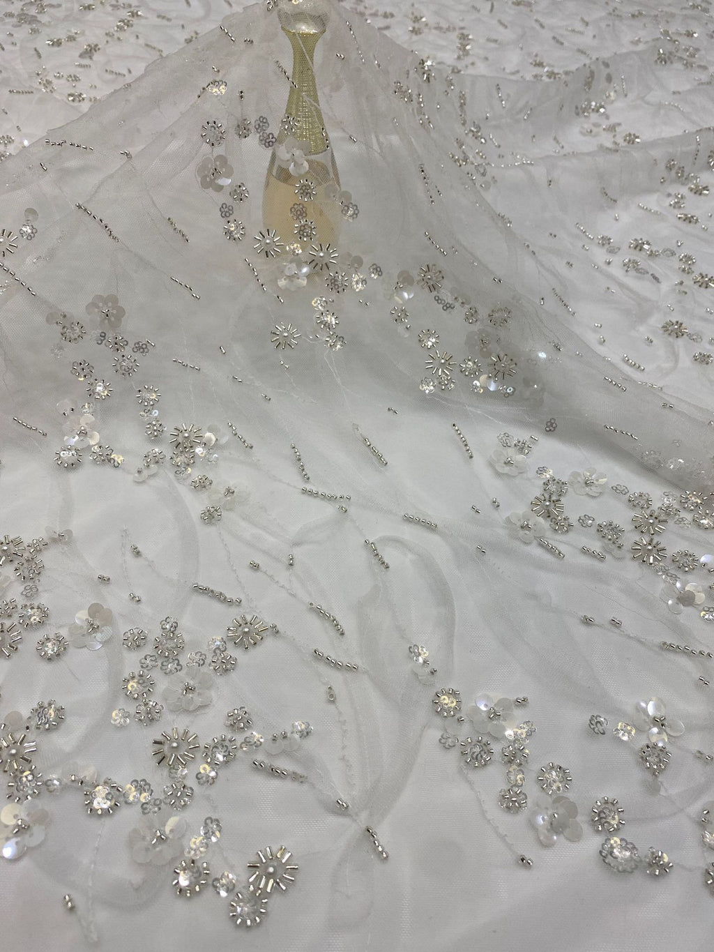 Angled detail of delicate beaded and sequined embroidery on sheer ivory fabric