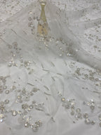 Angled detail of delicate beaded and sequined embroidery on sheer ivory fabric